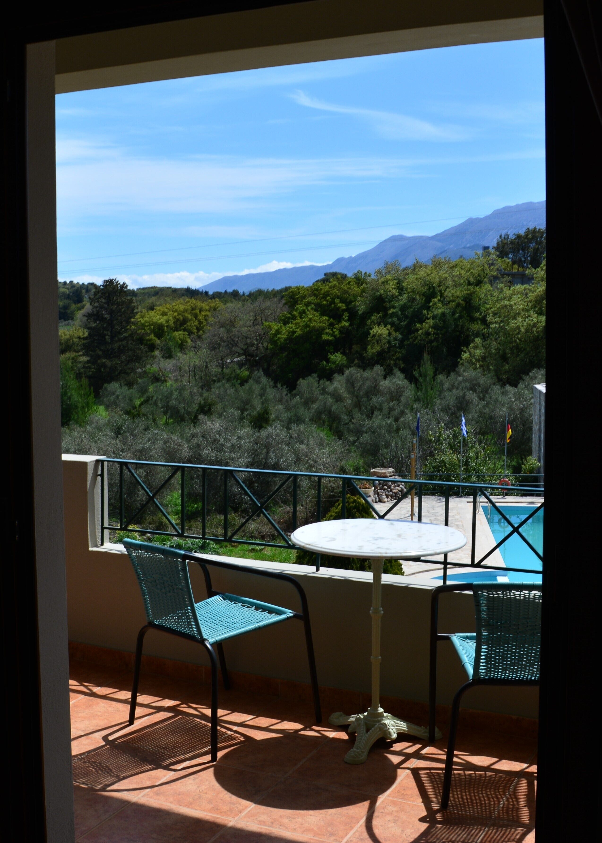 A balcony with a table and chairs, a pool, and a mountainous landscape view.