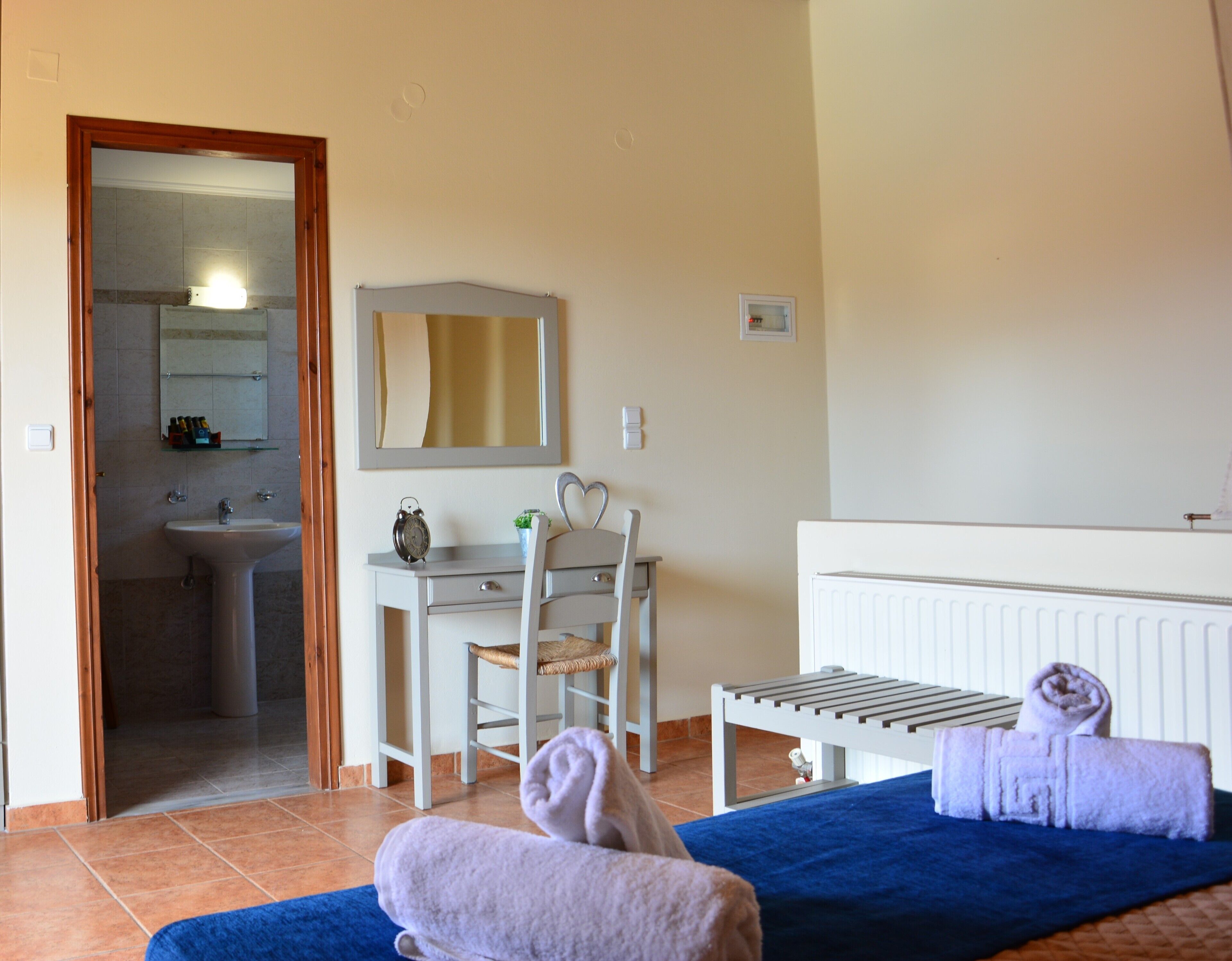 A room with a bed, a desk with a chair, a radiator, and a bathroom visible through an open door.