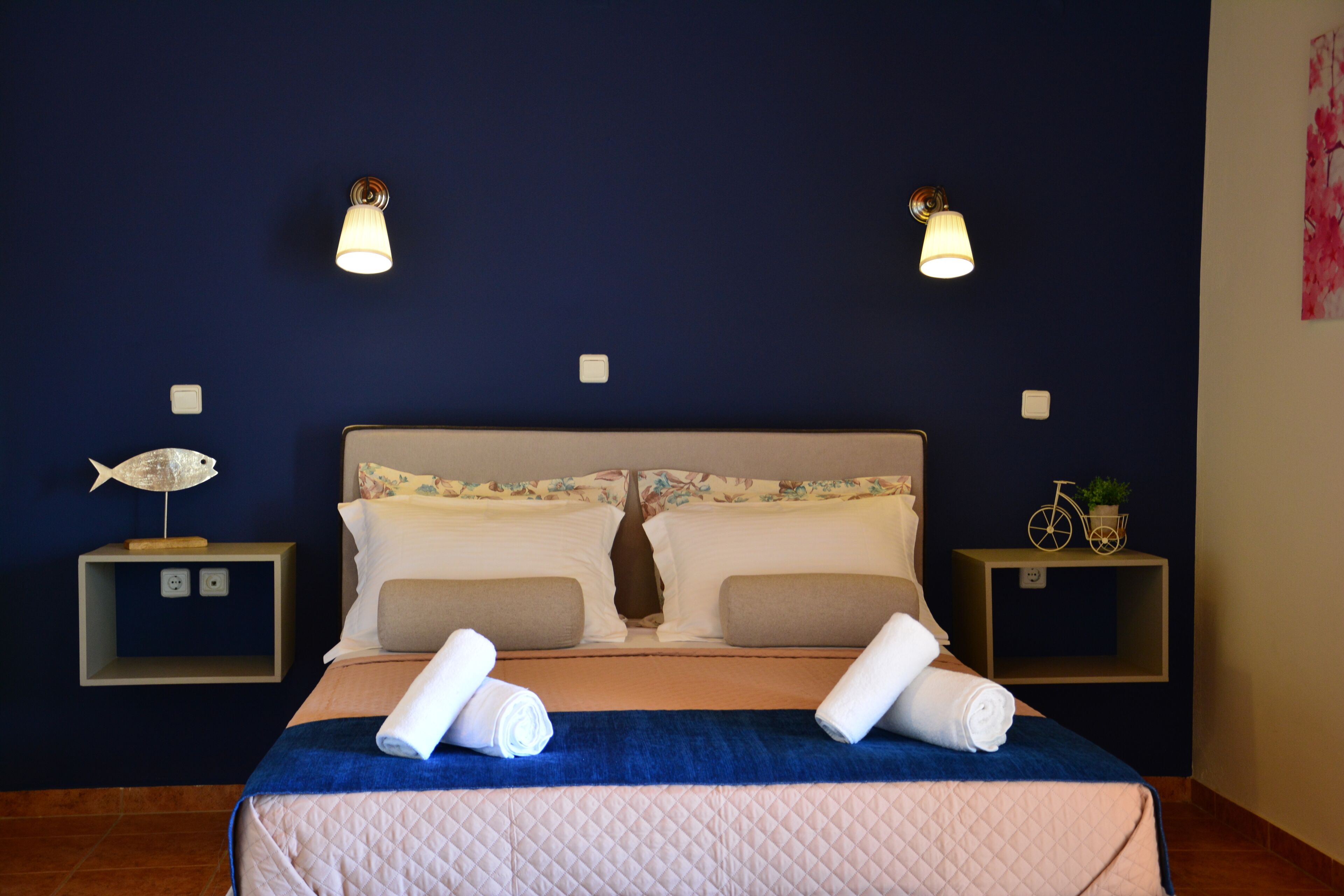 Hotelkamer met een bed, twee nachtkastjes, wandlampen, een decoratie van een vis en een decoratie van een fiets, plus een wandschildering.