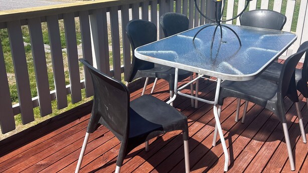 A wooden deck with a glass table and chairs, overlooking a grassy hill.