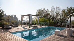 Una piscina en la azotea con cubierta de madera, sillas de descanso y una pérgola con toldo blanco.