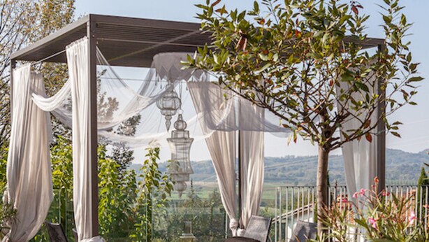 Un área de estar al aire libre con techo, una pérgola, sillas y una planta en maceta.
