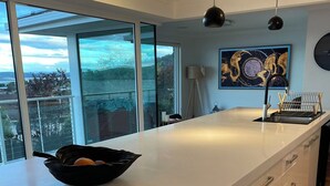 A modern kitchen with a large island, white cabinetry, and a view of the outdoors through large windows. - Lipscombe Escape panoramic views luxury and space (HOBART)