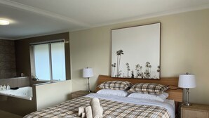 A hotel room with a large bed, two bedside tables with lamps, a large window, a bathroom with a bathtub, and a wall-mounted mirror. - Lipscombe Escape panoramic views luxury and space (HOBART)