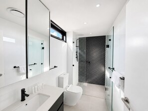 A modern bathroom with a large mirror, a white sink, a toilet, and a glass-enclosed shower area.