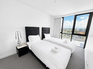A hotel room with two beds, a nightstand, a lamp, and a large window with a city view.