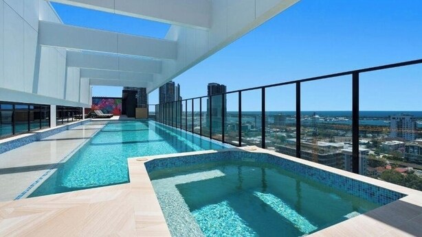 Ein Infinity-Pool auf dem Dach mit Blick auf die Stadt, Glasgeländern und einem klaren Himmel.