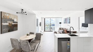 Eine moderne Küche mit Geschirrspüler, ein Essbereich mit rundem Tisch und Stühlen sowie eine Wohnarea mit Sofa und Fernseher.
