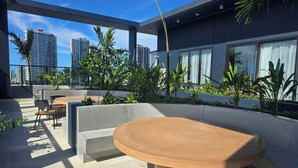 Eine Terrasse im Freien mit einem runden Tisch und Stühlen, umgeben von Grünpflanzen und mit Blick auf eine Stadtlandschaft.