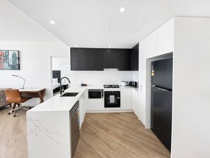 Une cuisine moderne avec des meubles blancs, un réfrigérateur noir et un plancher en bois.