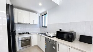 Ett modernt kök med vita skåp, ett kylskåp i rostfritt stål, en mikrovågsugn, en ugn och en diskmaskin.