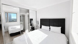 Ett modernt hotellrum med en stor säng, en spegel, ett nattduksbord och utsikt genom ett fönster.