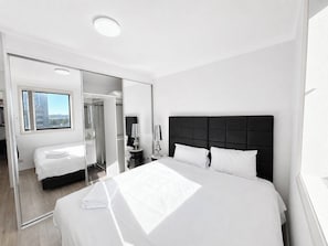 A modern hotel room with a large bed, a mirror, a bedside table, and a view through a window. - 7 Min to Train: Central Parramatta 2BR + Parking (Parramatta)