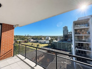 Un balcon offrant une vue dégagée sur le paysage urbain, avec des bâtiments et une colline visible au loin.