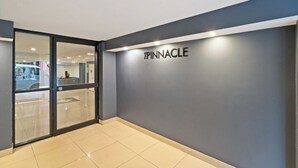 En modern hotellentrél med en glasdörr, en mörkgrå vägg och ordet ”PINNACLE” upplyst på väggen.