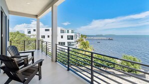 A balcony with a view of the sea, a modern building, and a wooden chair. - New Oceanside Paradise with Pool and Waterfront Views! (Key Largo)