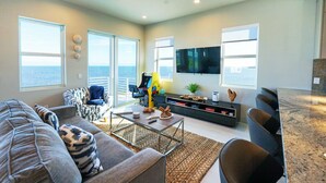 A modern living room with a large TV, comfortable seating, a coffee table, and a view of the ocean. - New Oceanside Paradise with Pool and Waterfront Views! (Key Largo)