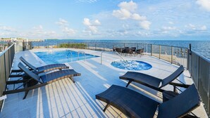 A pool area with lounge chairs and a hot tub, surrounded by a deck and a railing, overlooking the sea. - New Oceanside Paradise with Pool and Waterfront Views! (Key Largo)