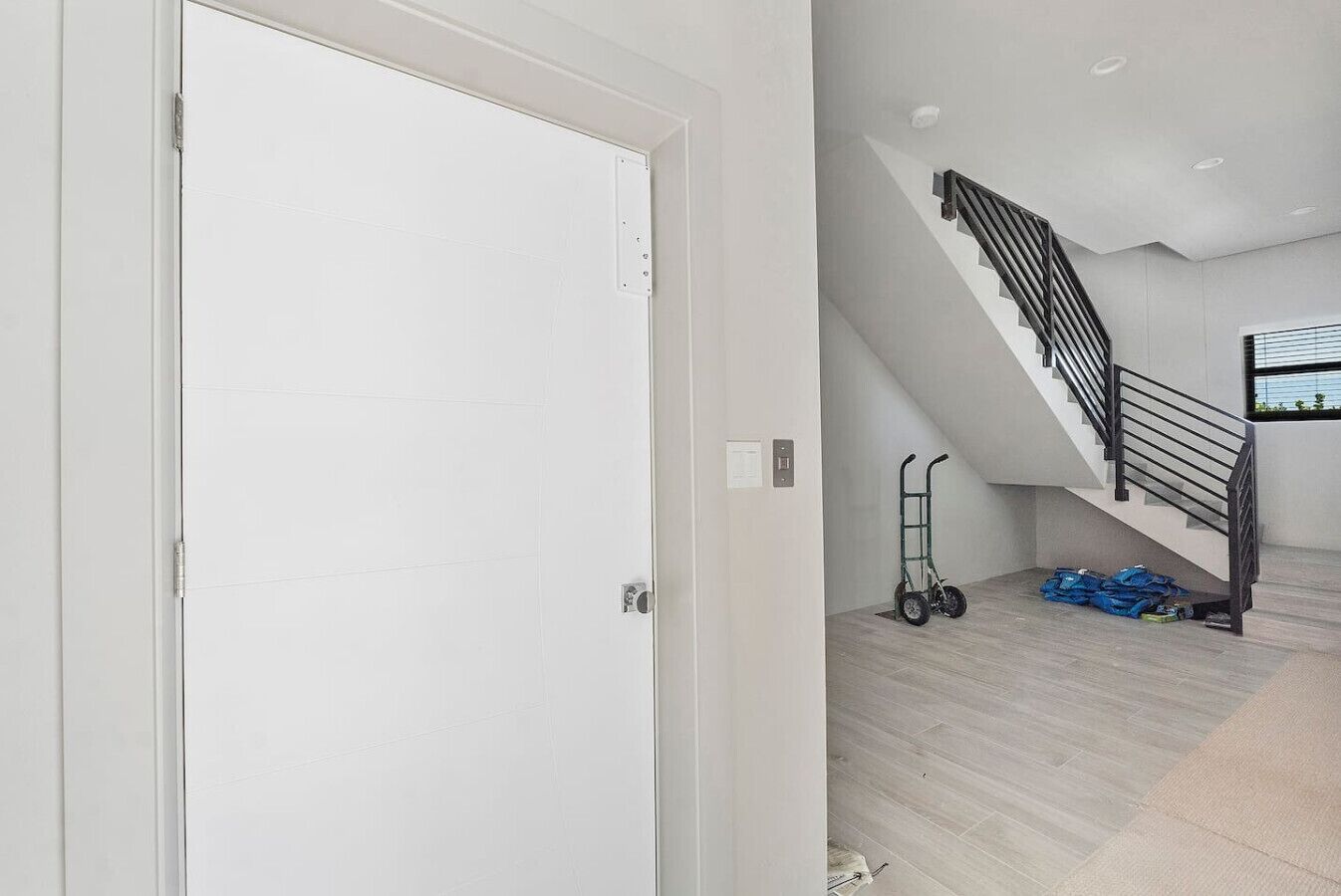 A modern interior with a staircase, a white door, and a cart with blue bags.