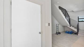 A modern interior with a staircase, a white door, and a cart with blue bags.