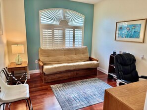 A cozy living room with a sofa, a chair, a desk, and a window with blinds.