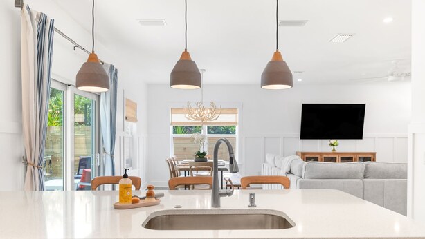 A modern kitchen with a central island, pendant lights, and a dining area with a chandelier. - Coastal Chic, Heated Pool, Beachside, Custom Bunk Room (St. Augustine)