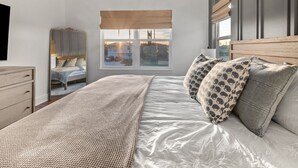 A bedroom with a large bed, a wooden headboard, a window with a view, a wardrobe, and a bedside table. - Coastal Chic, Heated Pool, Beachside, Custom Bunk Room (St. Augustine)