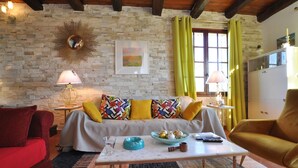 A cozy living room with a stone wall, a sofa with colorful cushions, a coffee table with a bowl and remote, and a red couch. - Awesome home in Saint-Laurent-du-Verdo (Saint-Laurent-du-Verdo)
