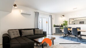 A modern living room with a black sectional sofa, a wooden coffee table, and a dining area with a blue rug. - #268 Marvellous Villa Sapphire by Home Holidays (Albufeira)