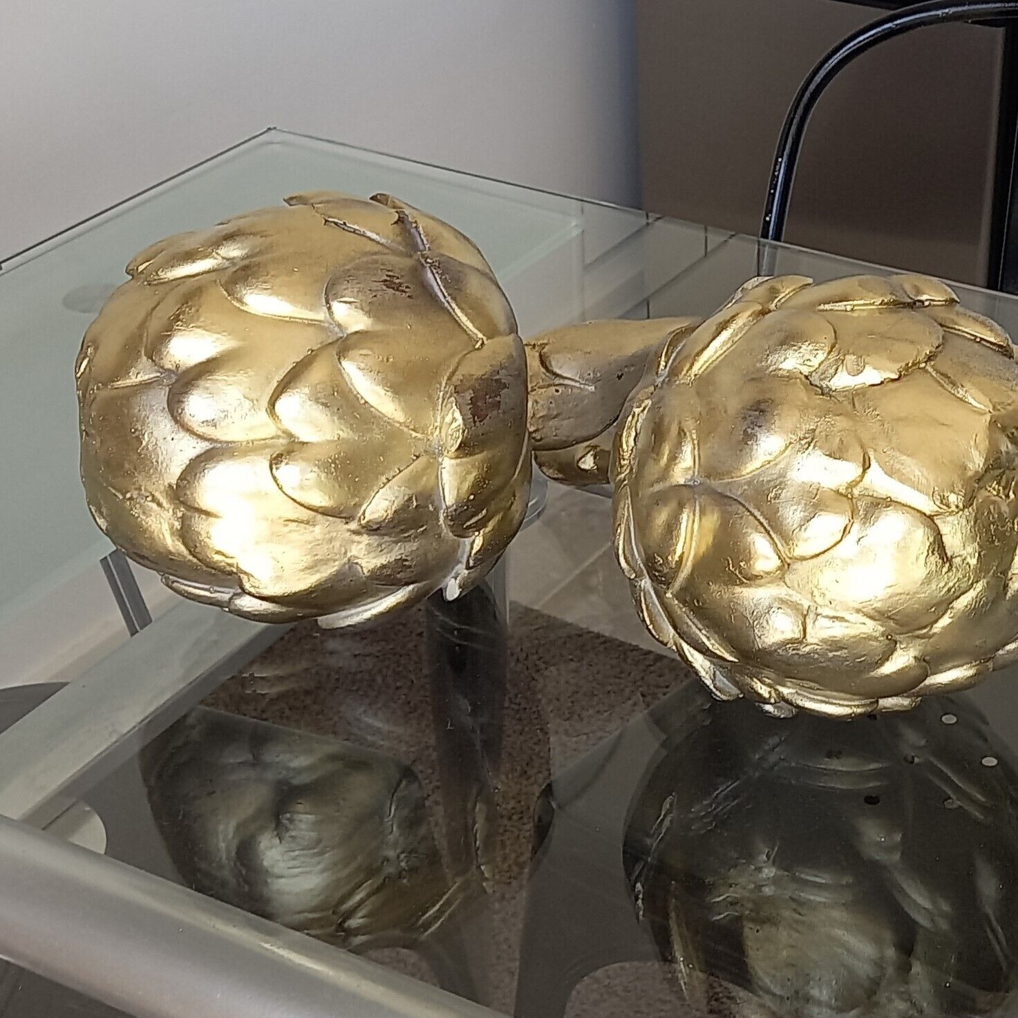 Two golden artichoke sculptures on a glass table.