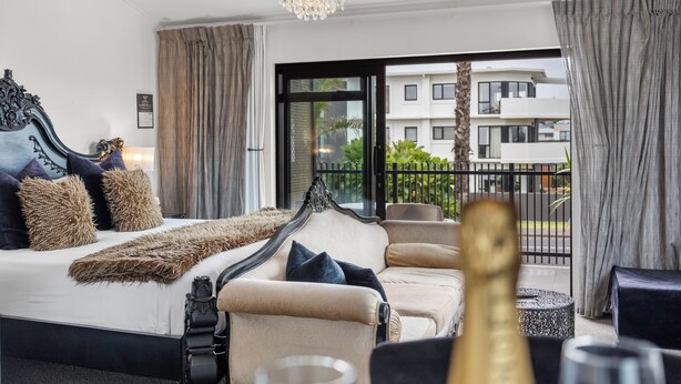 A modern hotel room with a large bed, a sitting area, and a balcony with a view of the city. - Orewa Beachcomber  (Orewa)