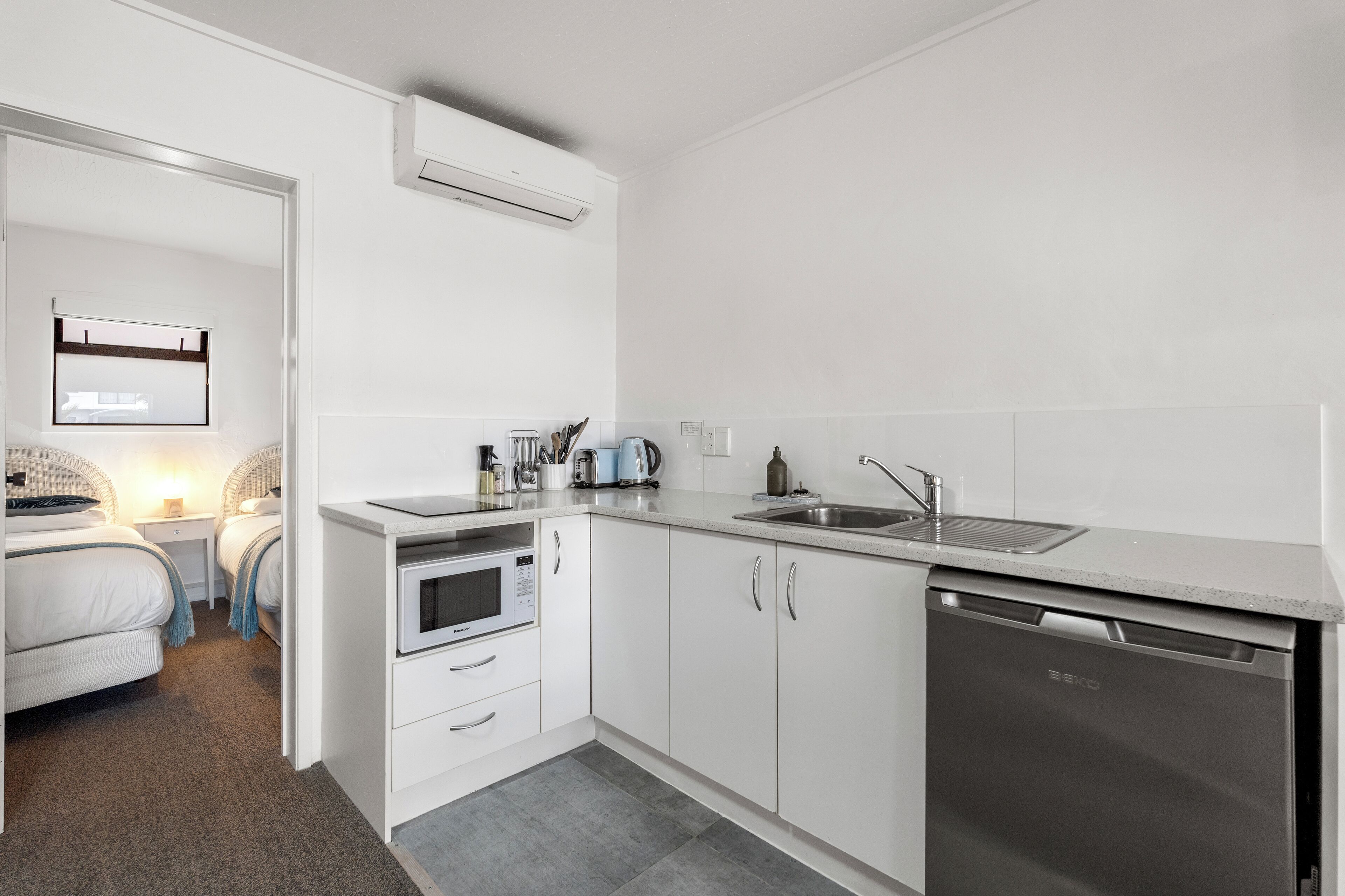 A compact kitchen with white cabinetry, a built-in microwave, a dishwasher, and a countertop with a sink.