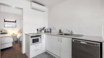 A compact kitchen with white cabinetry, a built-in microwave, a dishwasher, and a countertop with a sink.