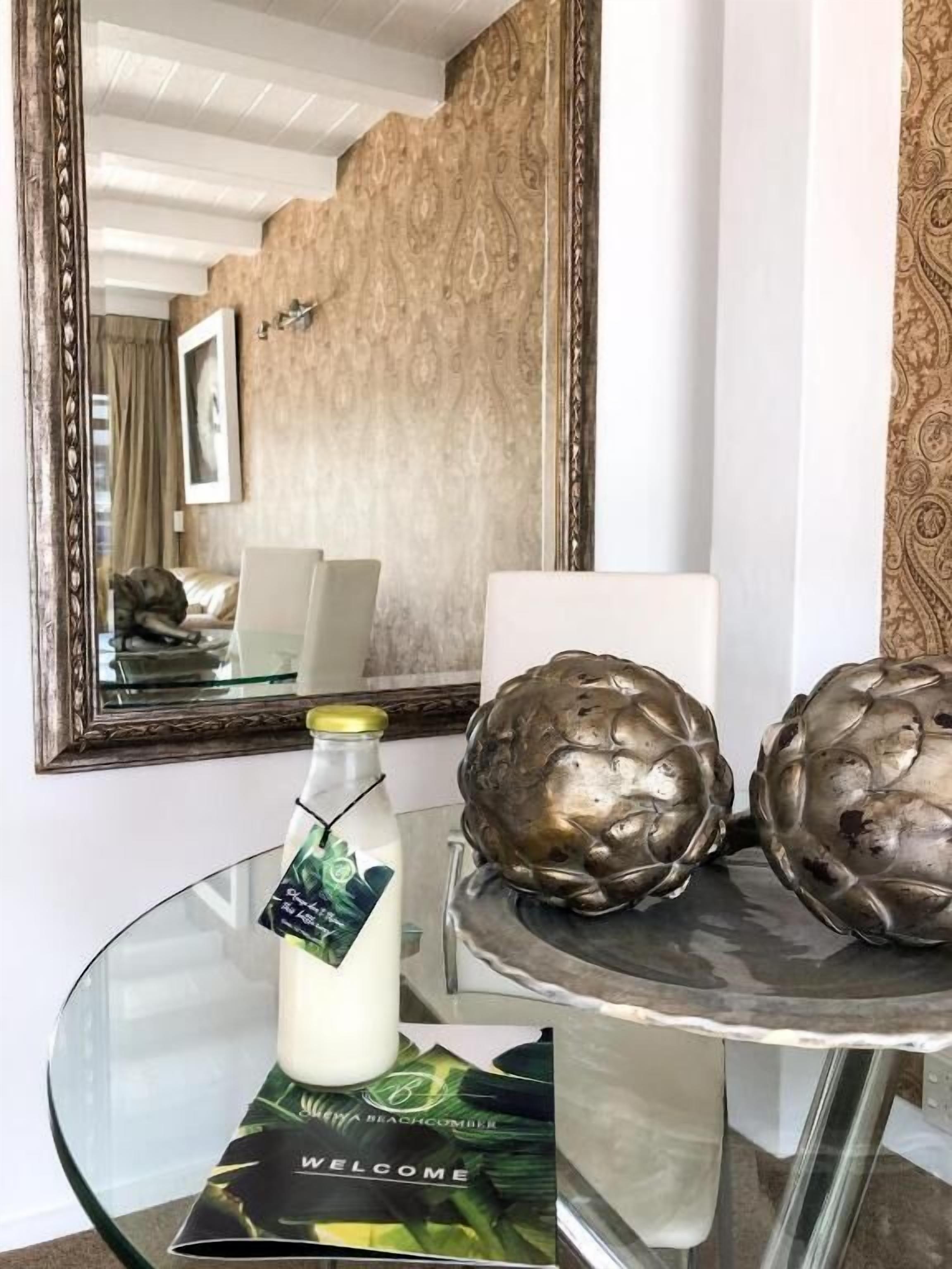 A glass table with a bottle and a welcome card, a mirror, and a patterned wall.