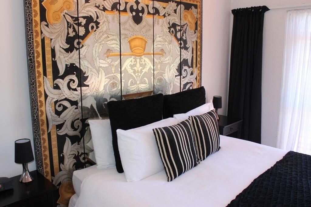 Hotelkamer met een groot bed, zwart-wit gestreepte kussens en een decoratief hoofdbord met een gouden ontwerp.
