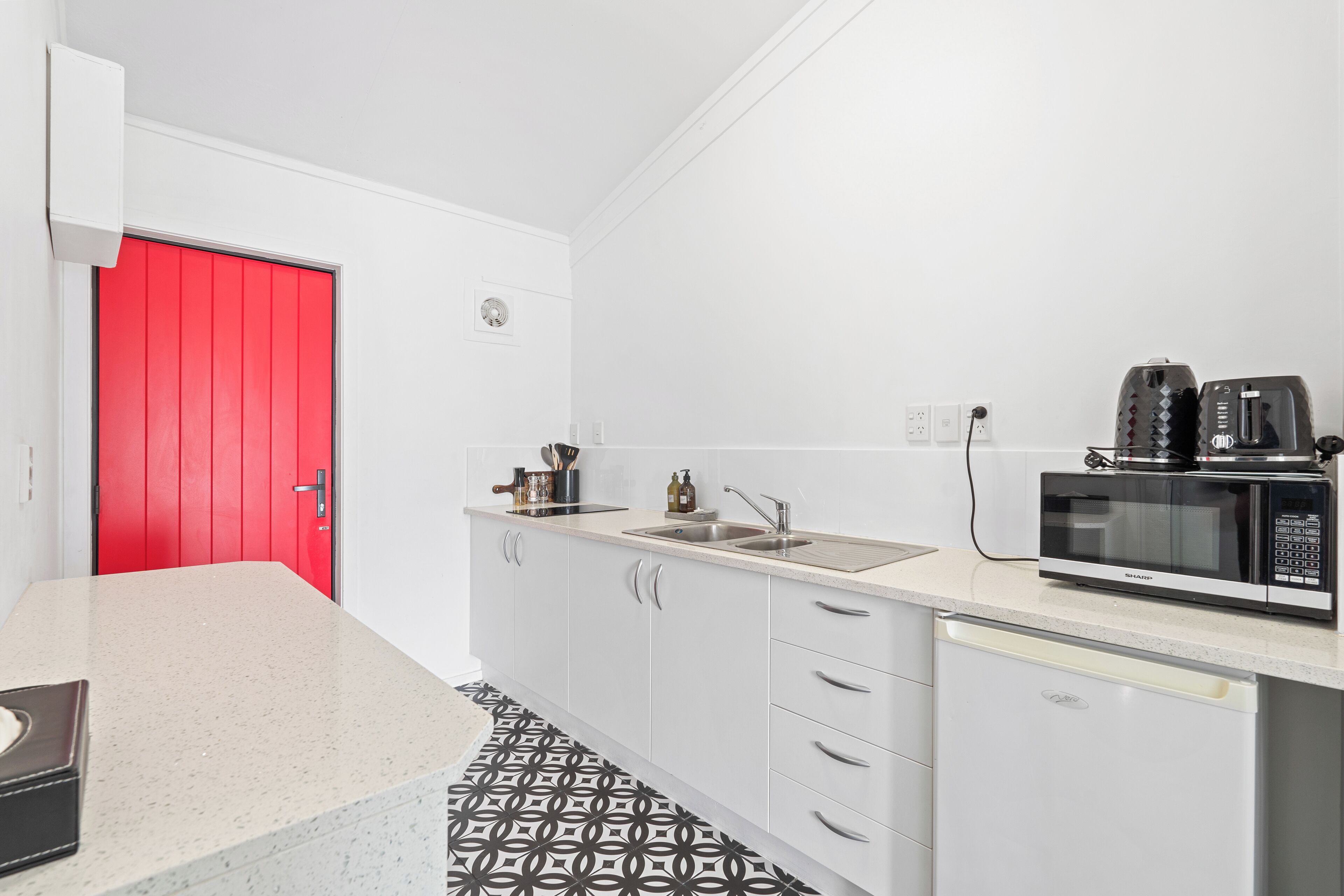 A compact kitchen with white cabinets, a red door, a microwave, and a dishwasher.