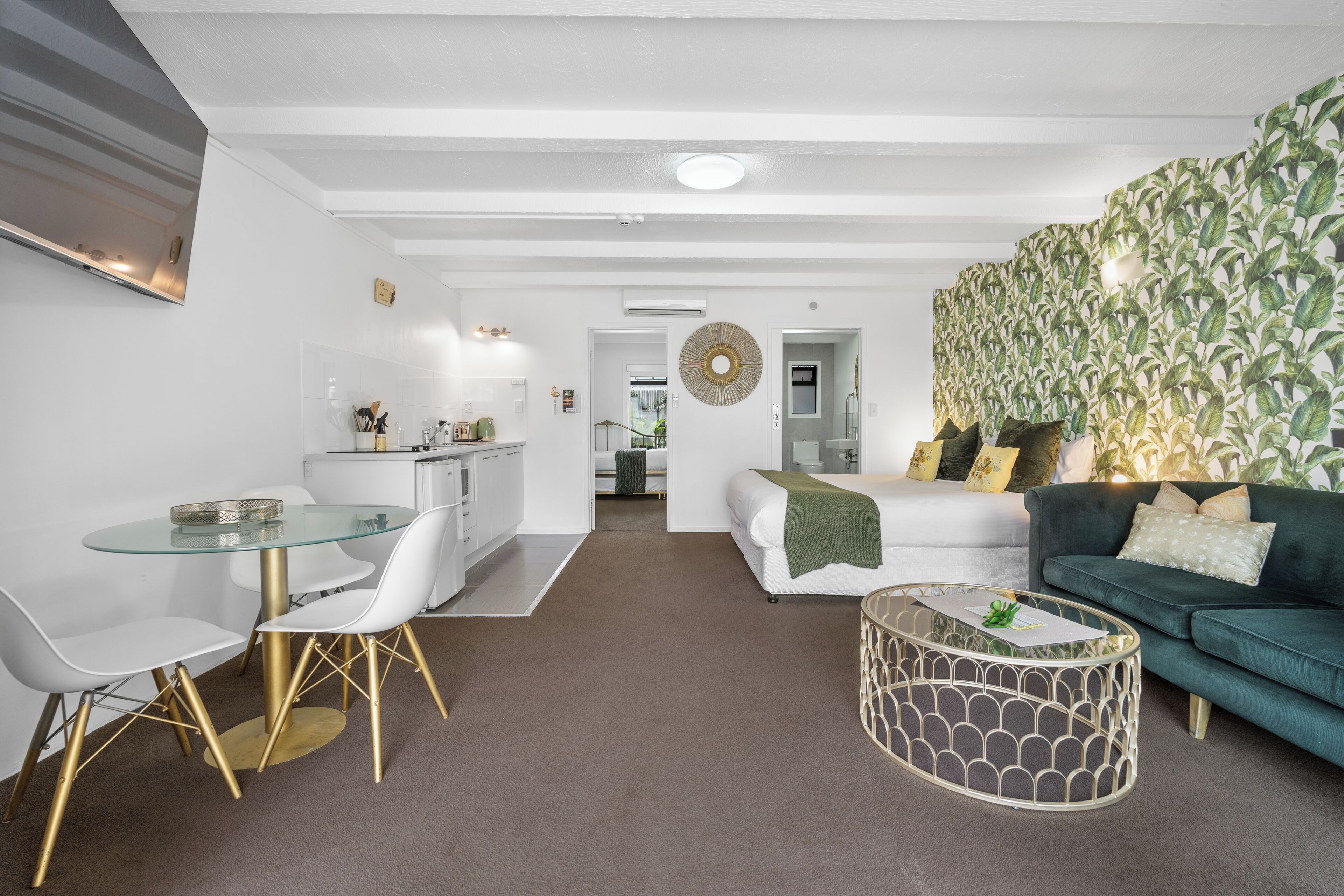 Una sala de estar moderna con una mesa de comedor de cristal, sillas blancas, un sofá verde y una pared estampada.