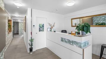 A reception area with a white counter, a mirror, and a potted plant.
