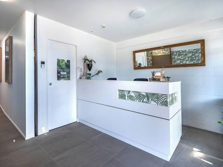 Un espace d’accueil avec un comptoir blanc, un miroir au-dessus et une porte sur la gauche.