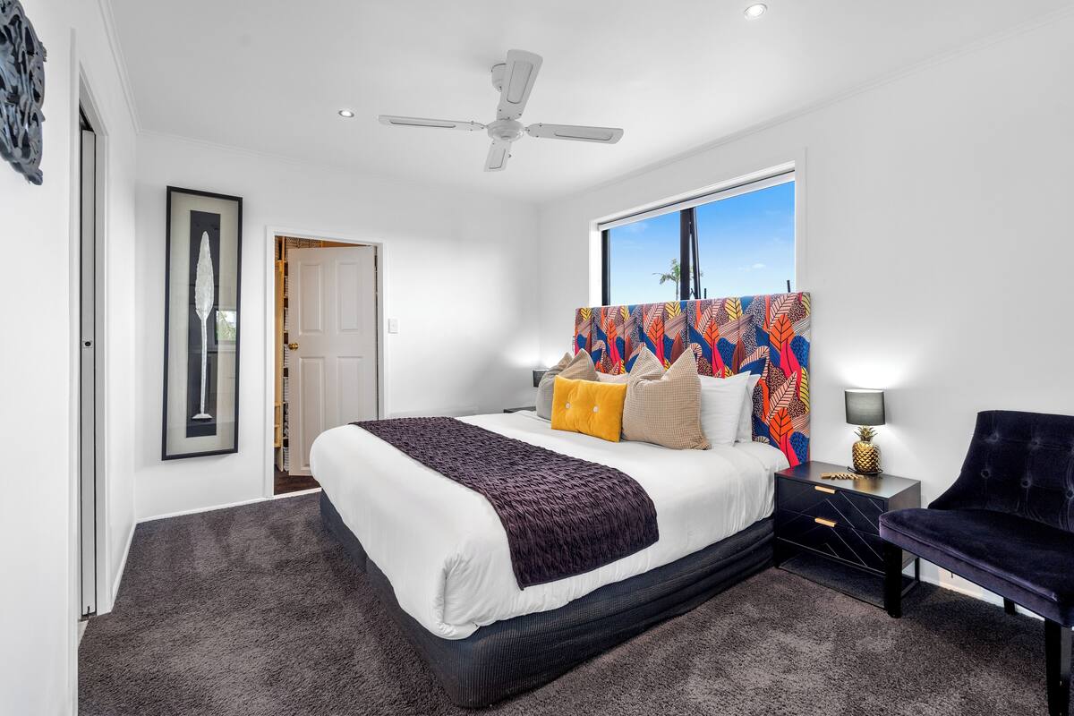 Ein Schlafzimmer mit Bett, Nachttisch, Sessel, Deckenventilator und Fenster mit Aussicht.