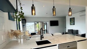 A modern kitchen with a central island, built-in dishwasher, and pendant lighting. - Orewa Beachcomber  (Orewa)