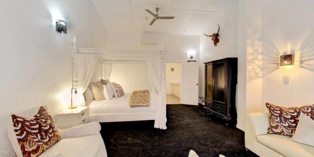A bedroom with a canopy bed, a sofa, a TV, and a ceiling fan.