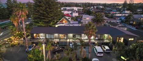 A modern hotel with a large parking area, multiple vehicles, and surrounding greenery.