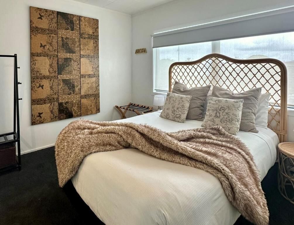 A bedroom with a bed, a large abstract painting, and a window with a view.