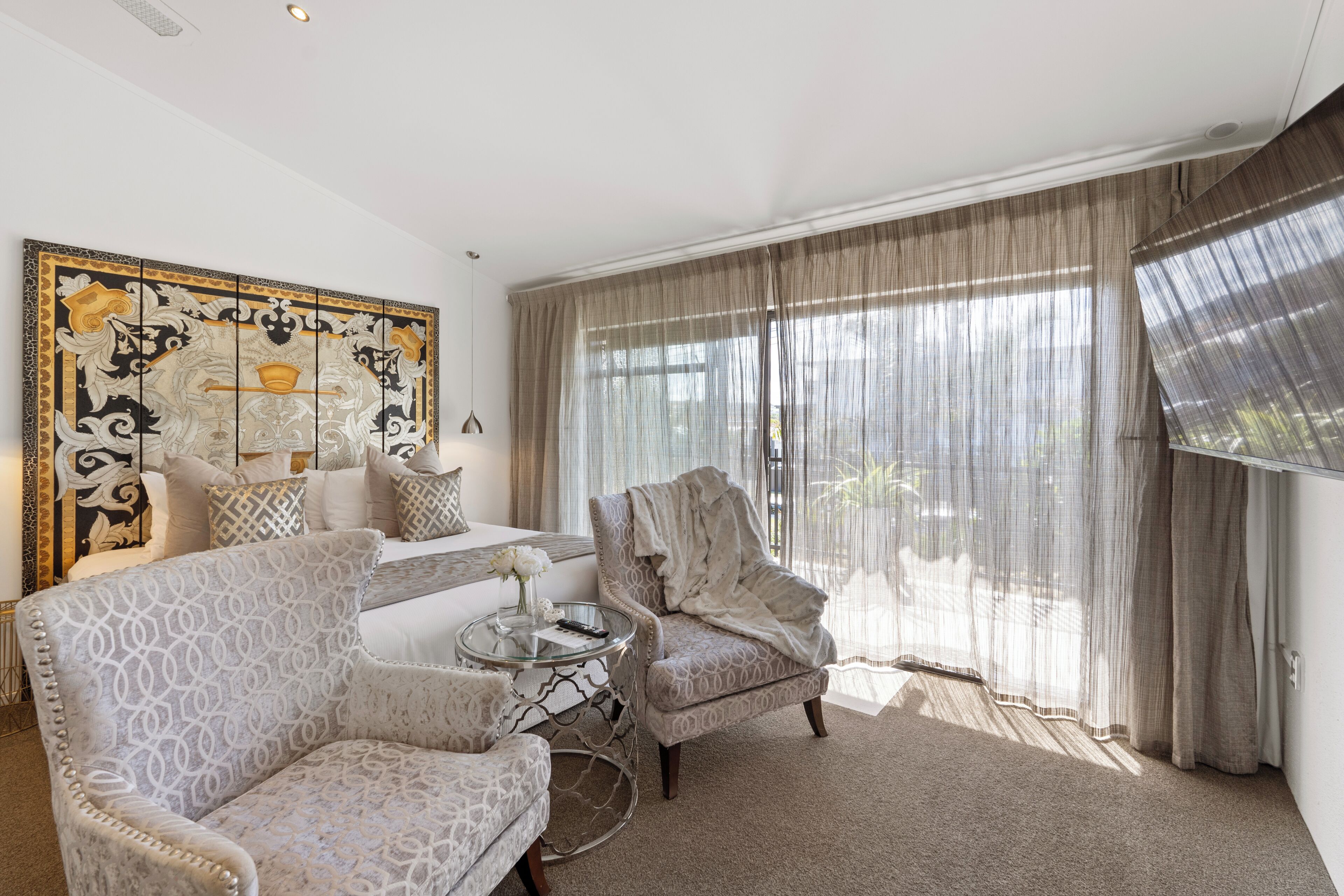 A living room with a sofa, two patterned armchairs, a glass coffee table, and a large decorative painting.