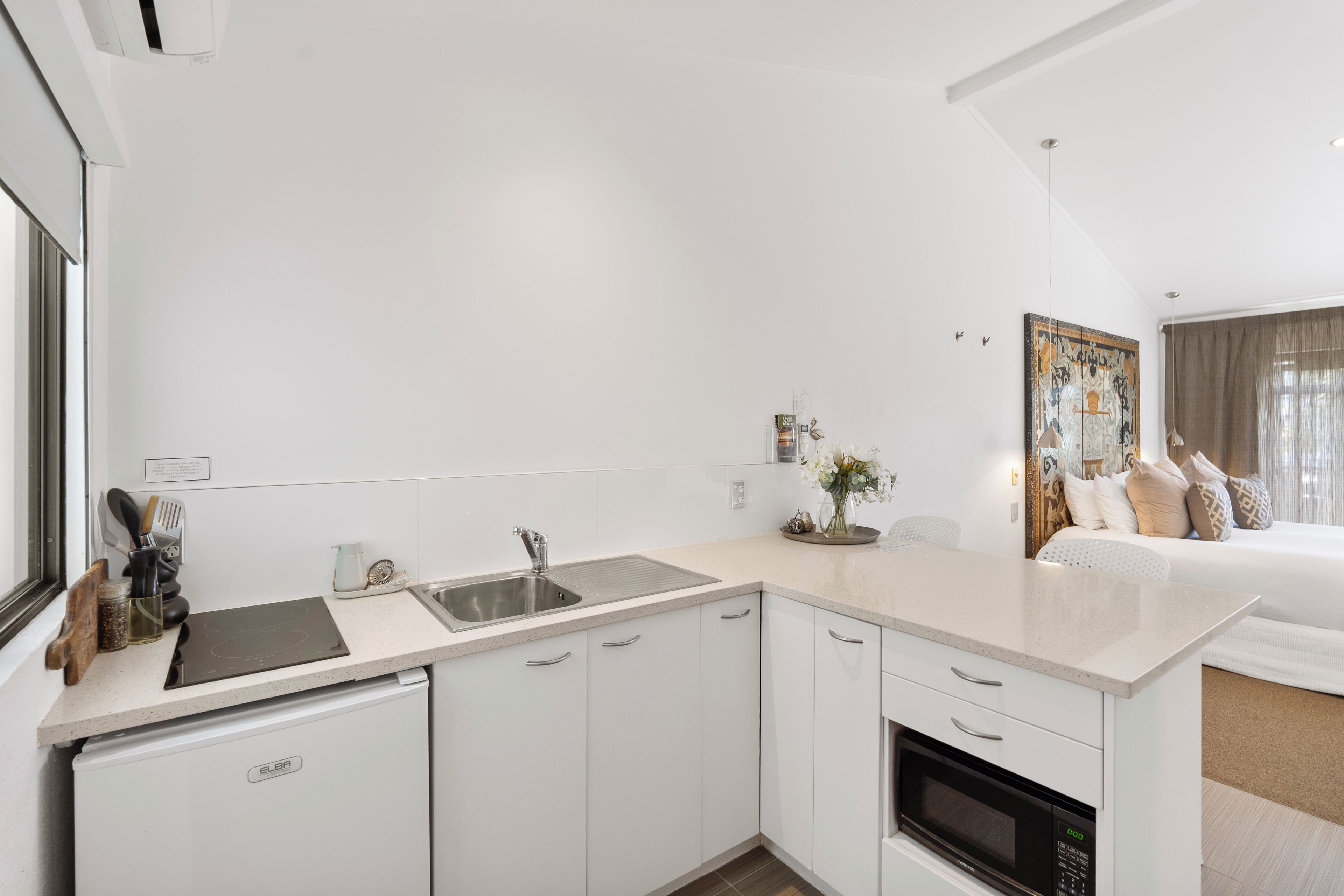 Una cocina moderna con armarios blancos, horno empotrado y pileta de acero inoxidable.