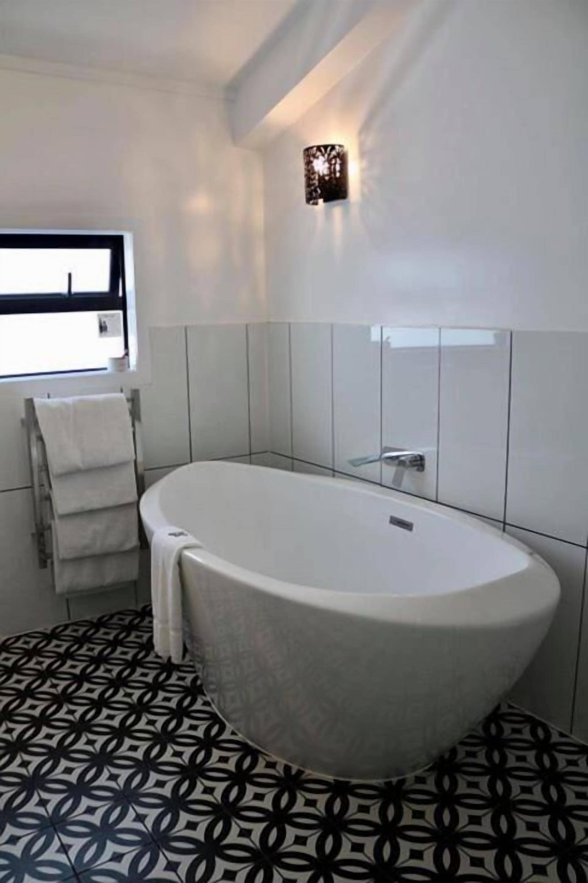 A modern bathroom with a freestanding bathtub, white tiled walls, and a patterned floor.