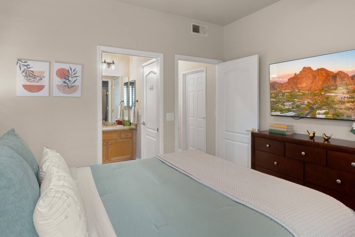 A bedroom with a bed, dresser, and a TV displaying a landscape.