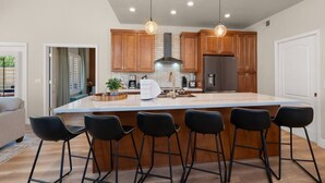 A modern kitchen with wooden cabinets, a stainless steel refrigerator, and a central island with bar stools. - Scottsdal:  Pool , 2BR/2BTH - Elegant! (Scottsdale)