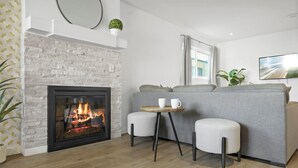A modern living room with a fireplace, a grey sofa, two white armchairs, and a small round table with cups. - Charming Condo in the Pico-Robertson area of LA/2-bed + 2.5 Bath/2 Parking spots (Los Angeles)